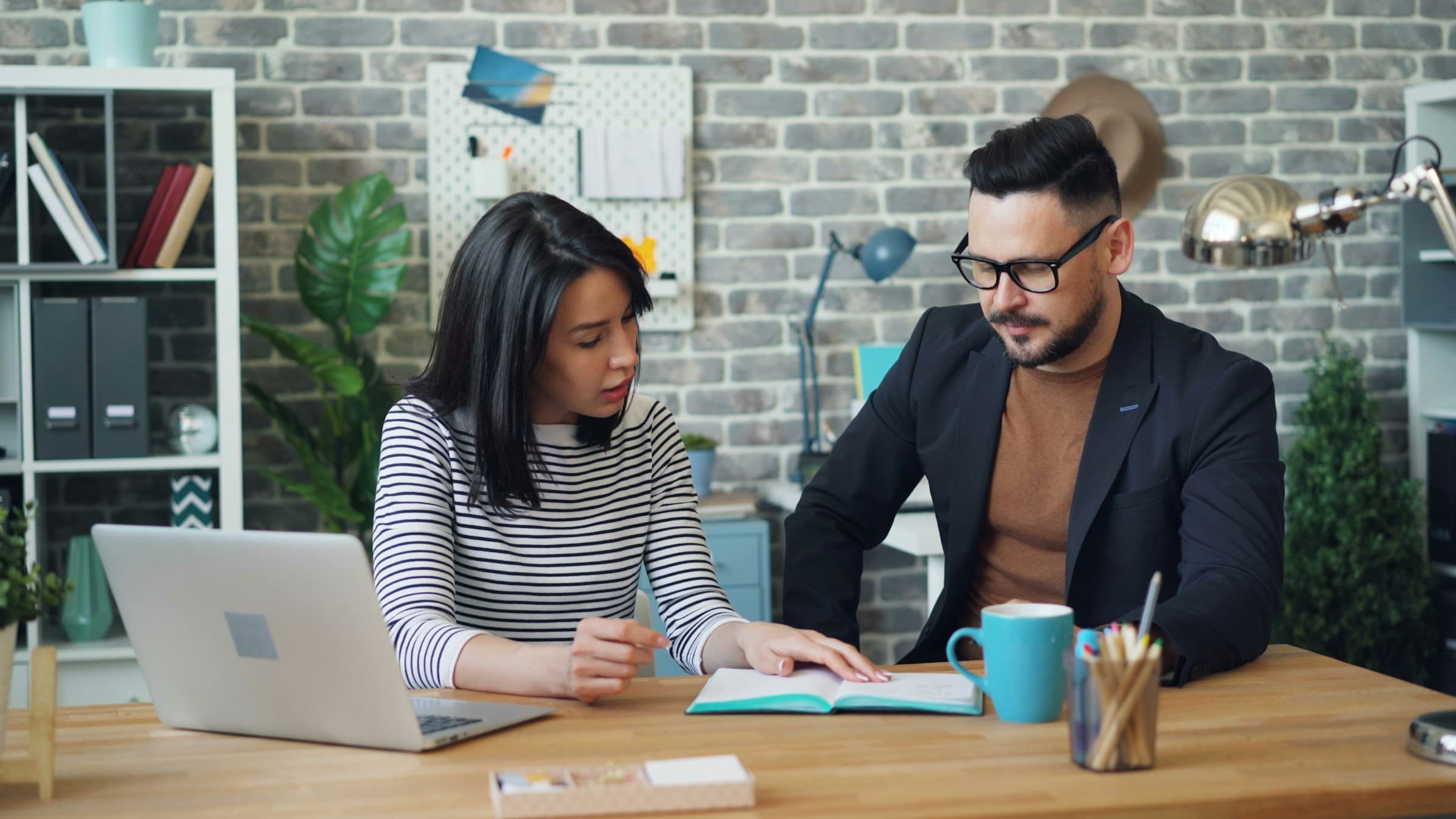 Two people reviewing notes together at a desk, with a laptop beside them