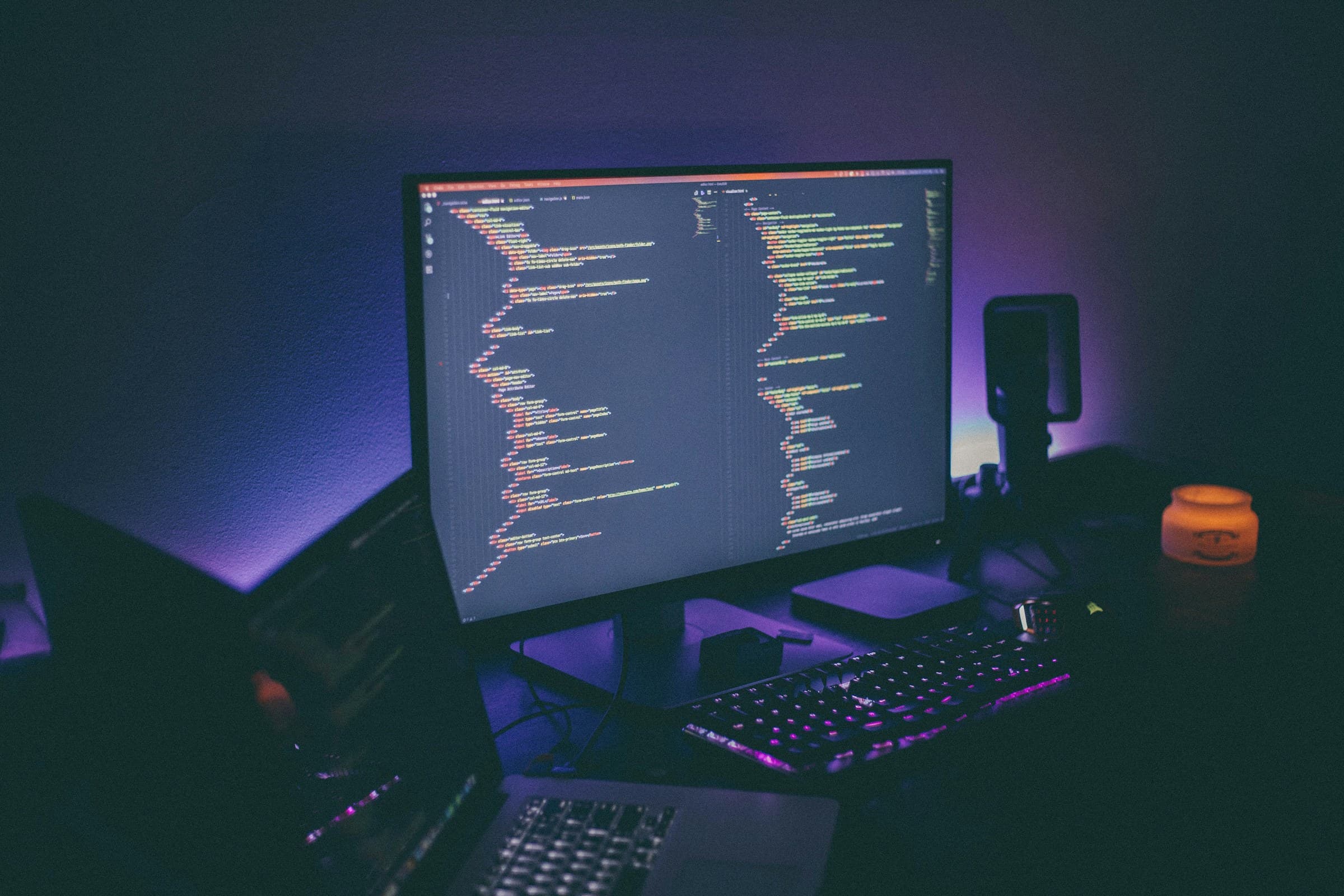 A monitor full of code on a desk lit by purple light