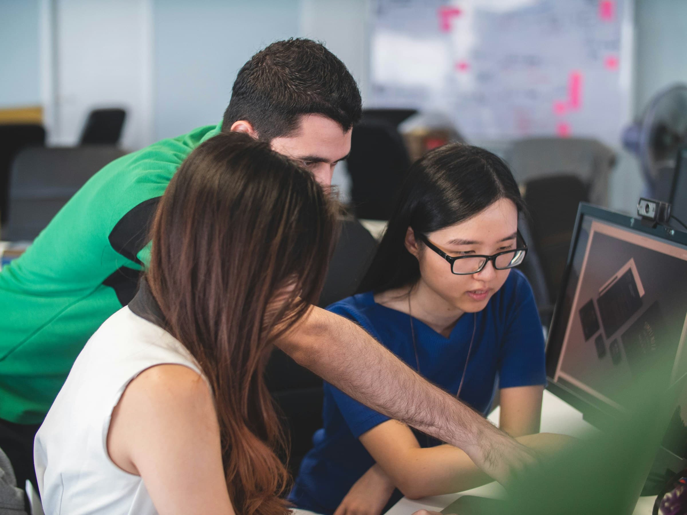 A man leans over to help two learners working at a computer