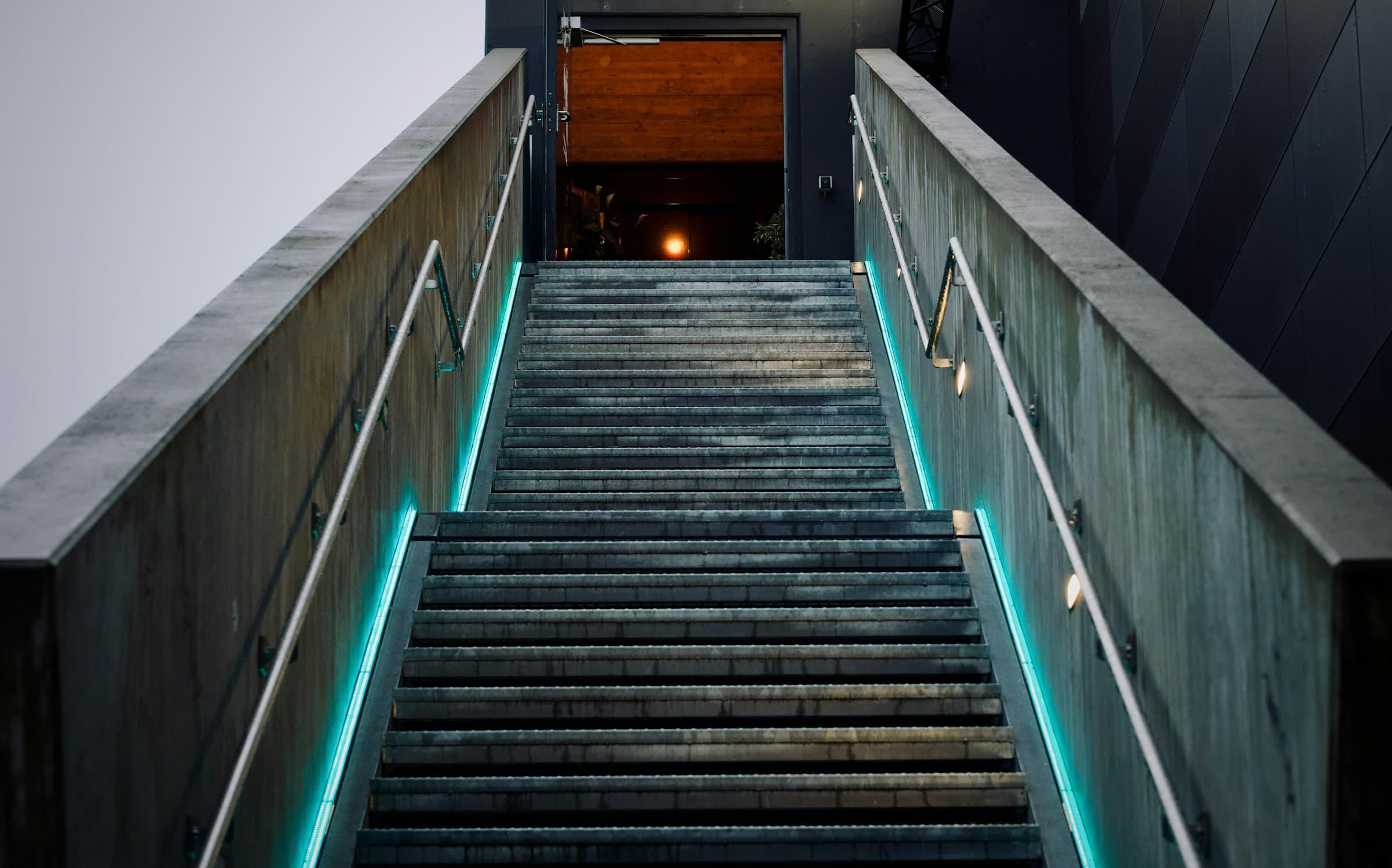 A concrete staircase lit by strips of cyan light, leading up to a glowing doorway