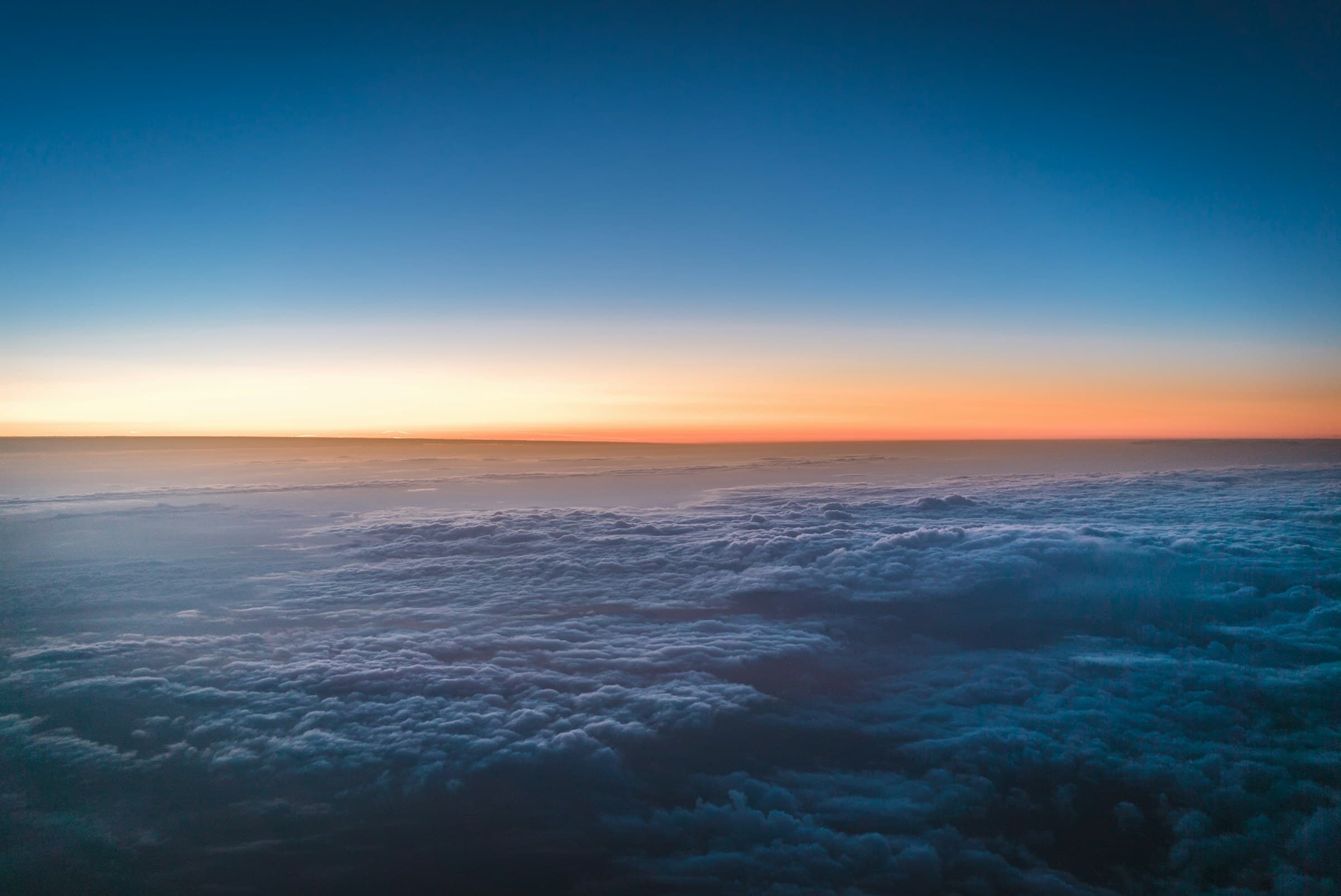 The view from above the clouds as dawn lights the horizon in orange and blue