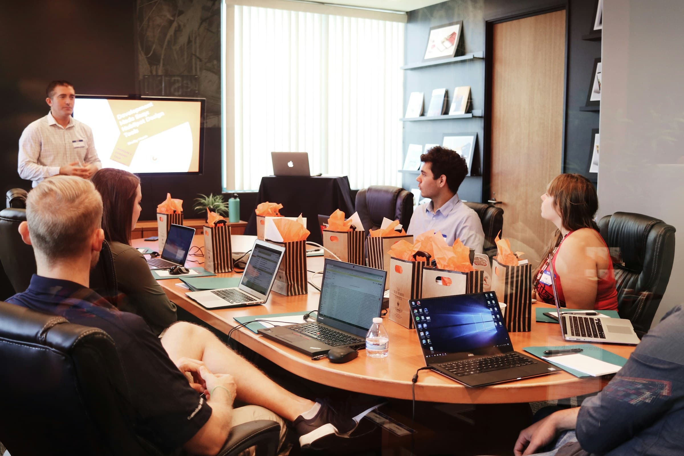 An instructor presents to a group seated around a conference table with laptops