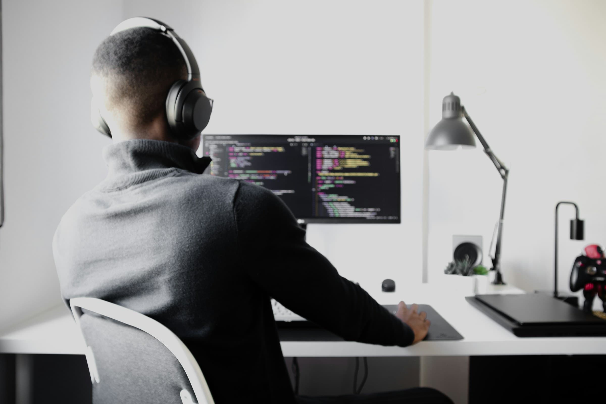 A person wearing headphones works on code at a tidy desk, seen from behind