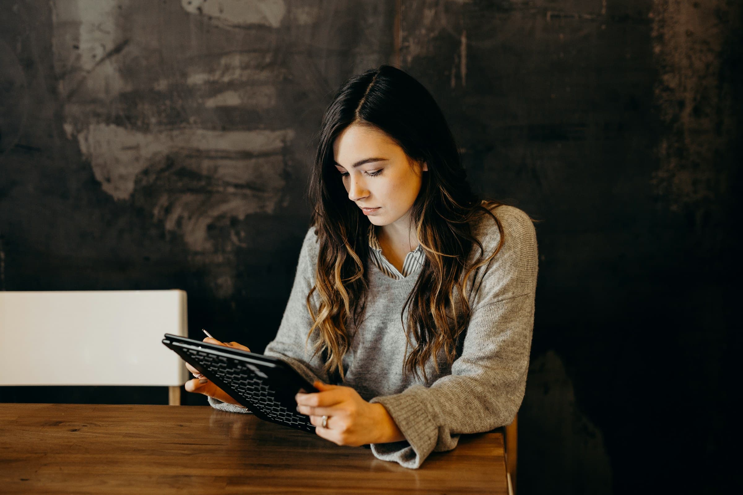 A woman studies on a tablet at a wooden table