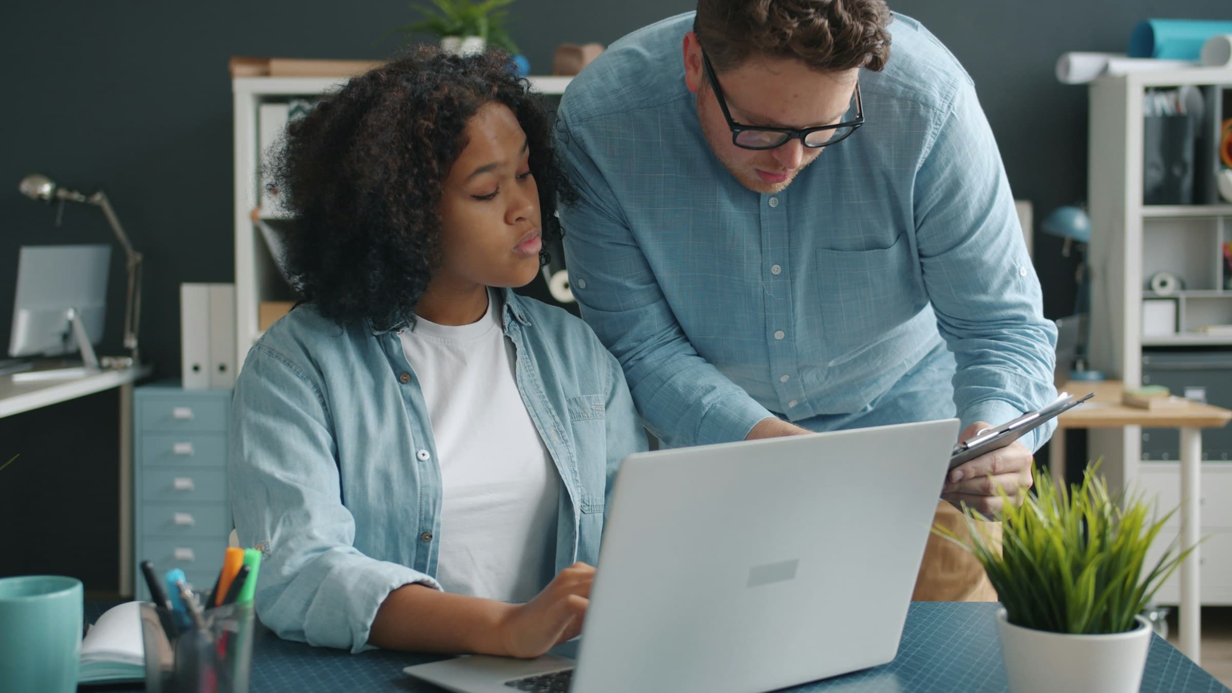 A man leans in to help a young woman with something on her laptop